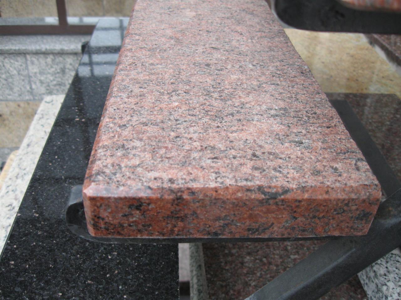 Czerwona płyta z polerowanego kamienia naturalnego o wyraźnej fakturze, prezentowana na ekspozycji z innymi materiałami wykończeniowymi.