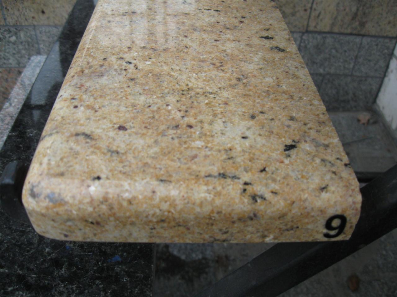 Przekrój blatu z jasnego, ziarnistego kamienia naturalnego z zaokrąglonym brzegiem, oznaczony numerem '9', prezentowany na ekspozycji.