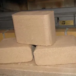 Trzy kostki brykietu drzewnego RUF ułożone przed kominkiem z żeliwną obudową i ceglanym obramowaniem.