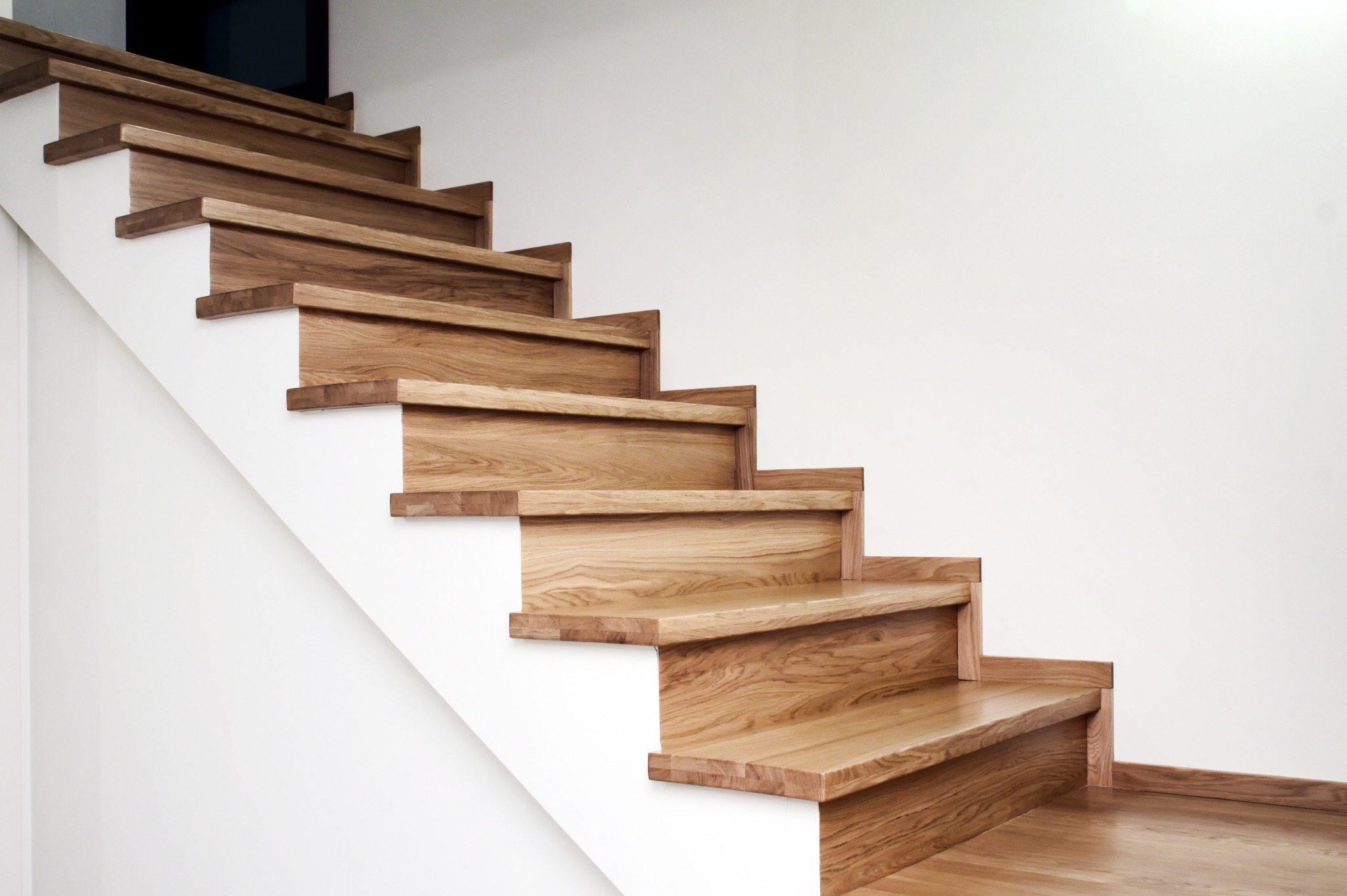 Nowoczesne schody drewniane z jasnego drewna, minimalistyczny design, białe ściany, naturalne oświetlenie, widoczne usłojenie drewna, eleganckie wykończenie.