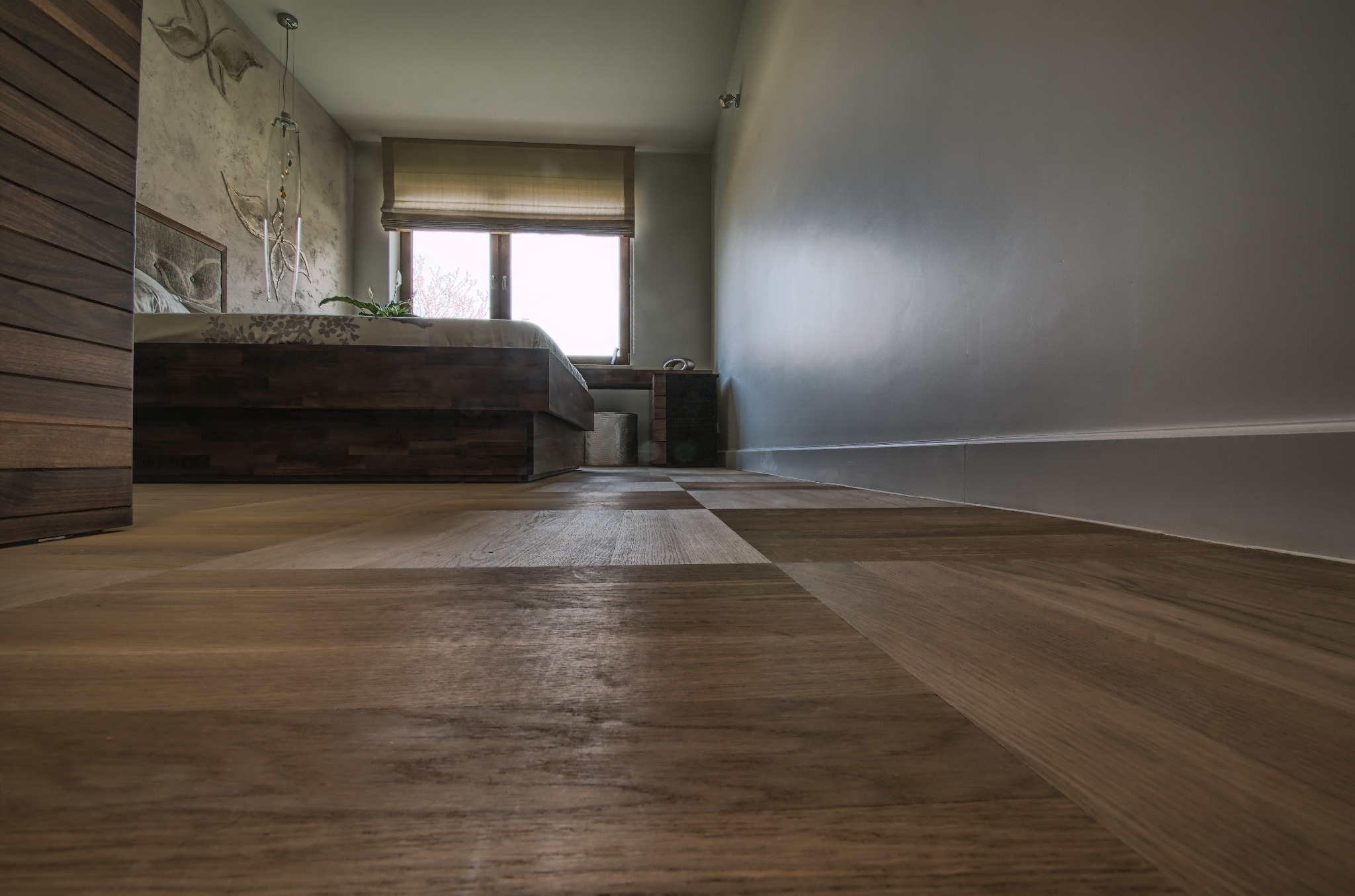 Nowoczesna sypialnia z parkietem ułożonym w szachownicę z ciemnego drewna. Widok z niskiej perspektywy podkreśla wzór podłogi i minimalistyczny wystrój wnętrza.