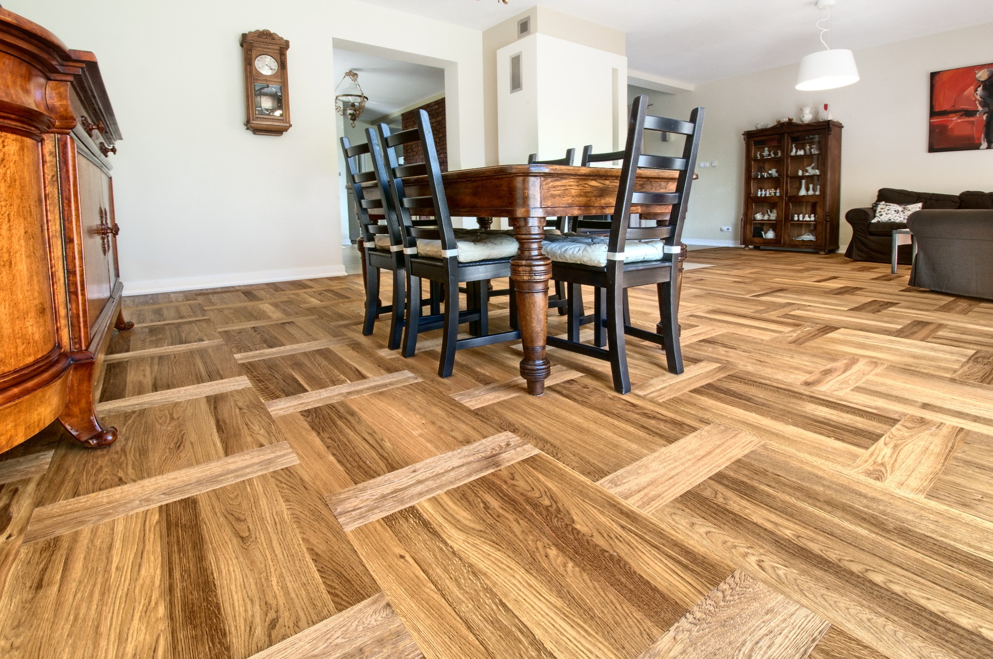 Parkiet ułożony w jodełkę francuską, zróżnicowany odcieniem drewna, w przestronnym salonie z meblami w stylu vintage i nowoczesnym oświetleniem.