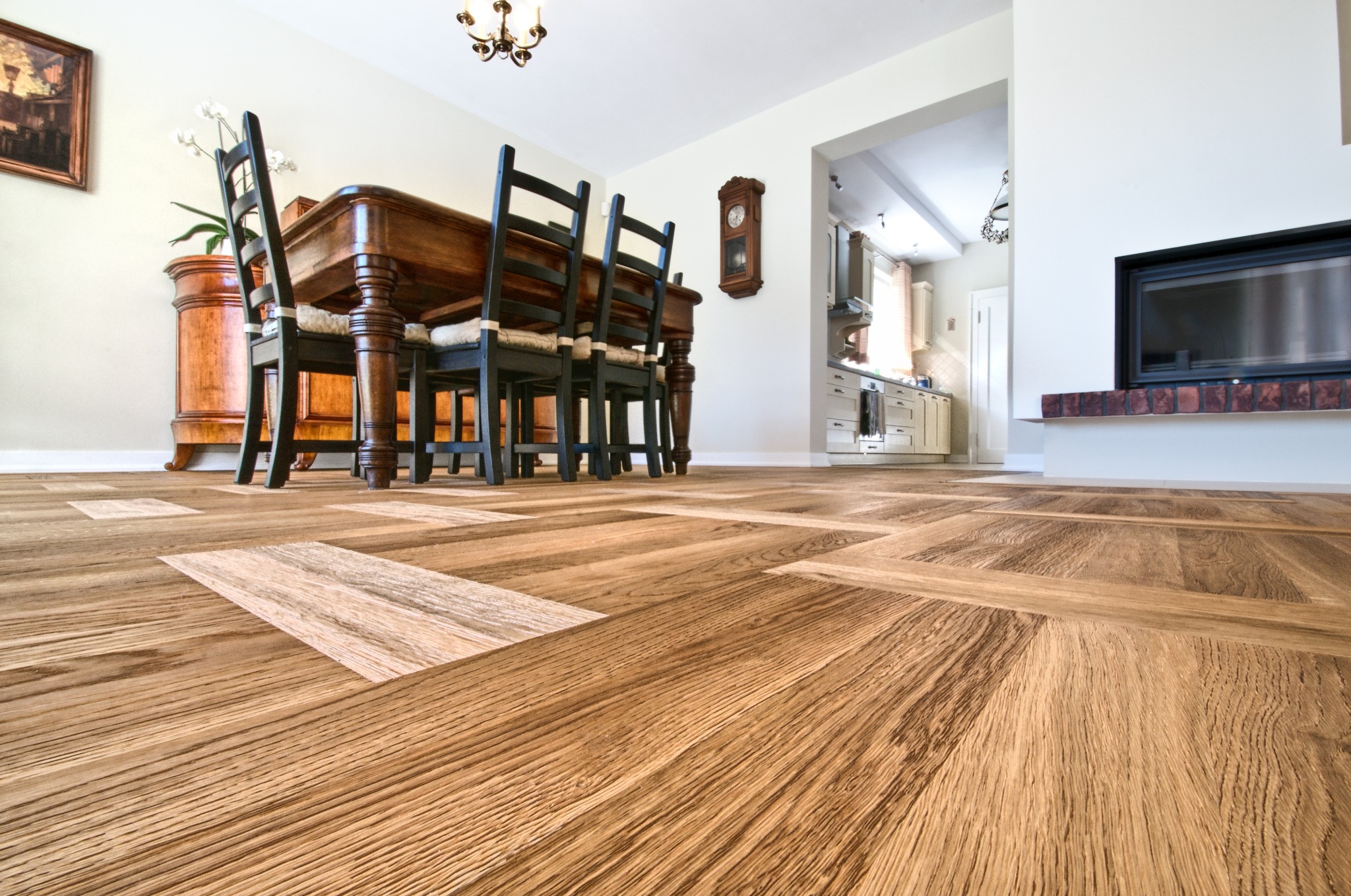 Parkiet w jodełkę francuską z jasnymi wstawkami, stół z krzesłami w tle, widok z niskiej perspektywy podkreślający wzór podłogi i wnętrze domu.