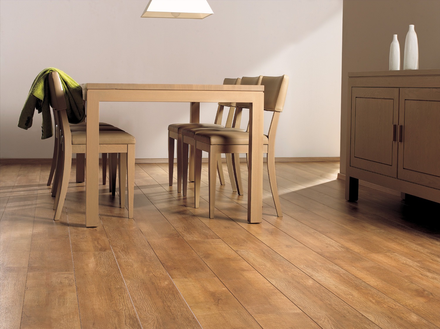 Jasnobrązowa podłoga z paneli, stół z krzesłami i komoda w tle. Widoczne naturalne światło podkreśla strukturę drewna. Minimalistyczny design wnętrza.