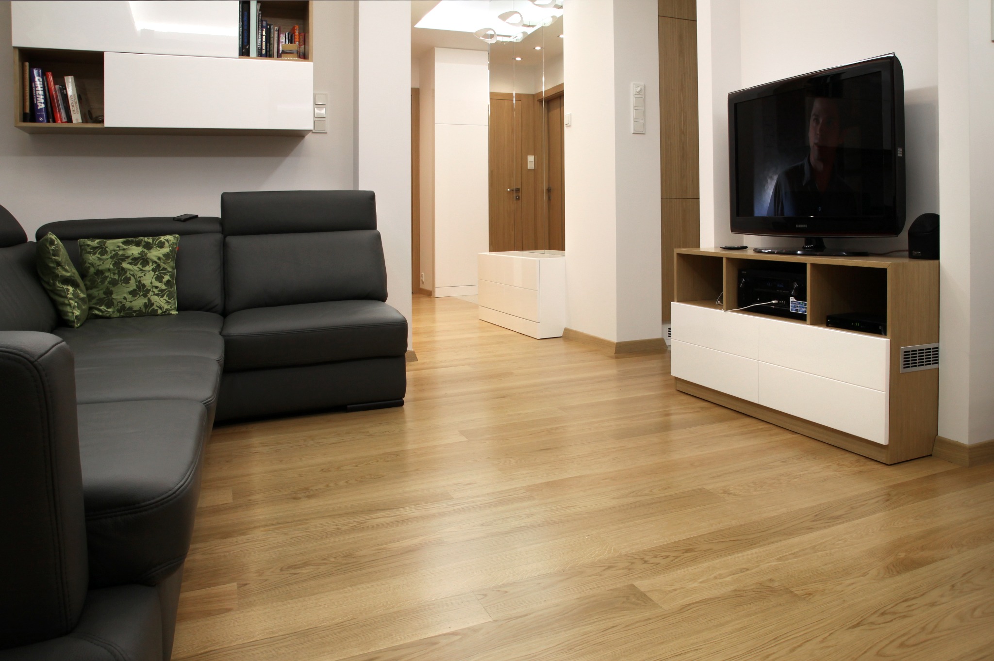 Jasna, drewniana podłoga w salonie z szarą sofą i białymi meblami. Widoczne delikatne usłojenie drewna i nowoczesny design wnętrza.