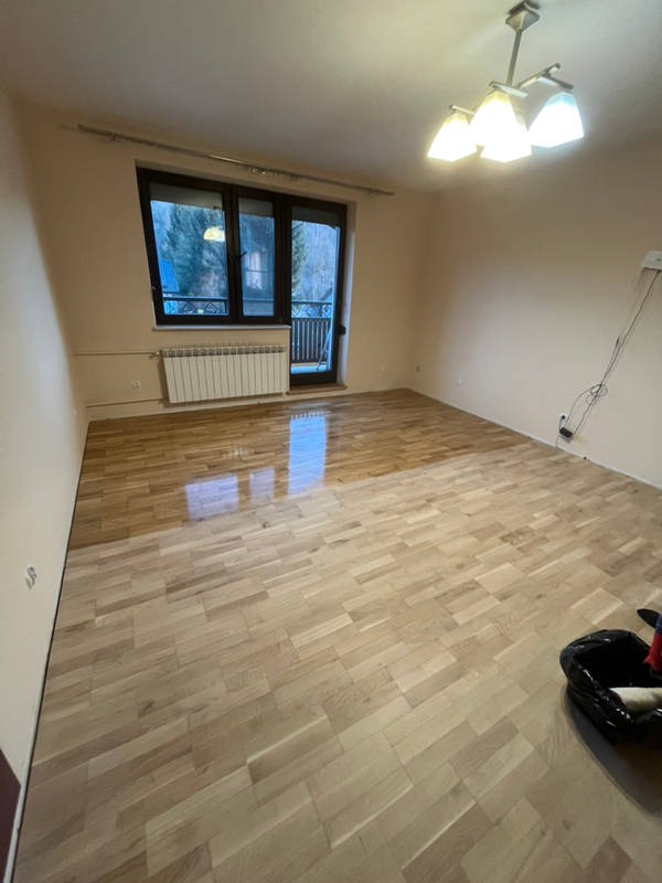 Parkiet w trakcie renowacji: połowa powierzchni wycyklinowana, druga w stanie surowym. Widoczne okno balkonowe i narzędzia pracy.