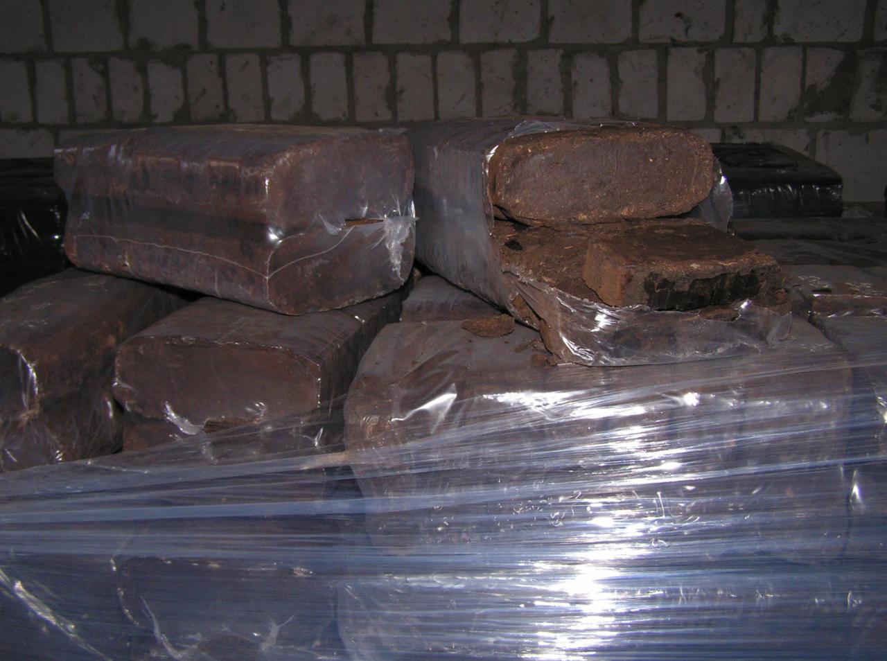 Ułożone w stos brykiety torfowe, częściowo rozpakowane z folii, na tle ściany z cegieł.