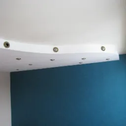 Pomieszczenie po odświeżeniu: biały sufit z dekoracyjnym, podwieszanym elementem i wpuszczonymi punktowymi lampkami, ściana pomalowana na intensywny, ciemny odcień niebieskiego, widoczne okno.