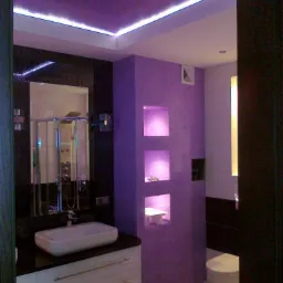 Fioletowa łazienka z podświetlanym sufitem, umywalką nablatową na szafce z szufladami i wnękami w ścianie z dekoracyjnym oświetleniem punktowym.