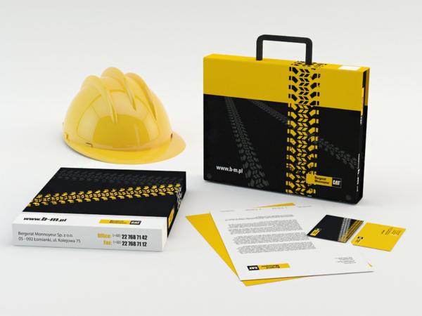 Żółty kask budowlany obok pudełek i wizytówek z motywem śladów opon i logo firmy Bergerat Monnoyeur, całość w czarno-żółtej kolorystyce.