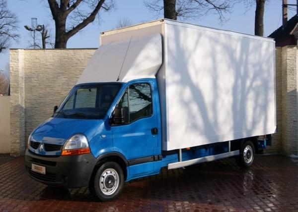 Niebieski samochód dostawczy Renault Master z białą zabudową kontenerową, zaparkowany na brukowanej powierzchni przed jasnym murem z dekoracyjną fakturą kamienia.