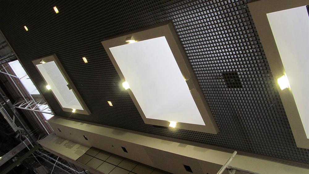 Sufit podwieszany z rastrową kratką i wpuszczonymi panelami świetlnymi, widok z dołu, oświetlenie punktowe.