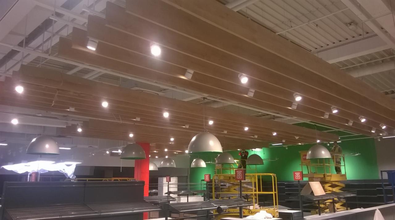 Montaż drewnianego sufitu rastrowego z oświetleniem w hali sklepu Kaufland Bielsko Biała, widoczny podnośnik nożycowy i pracownik w kombinezonie.