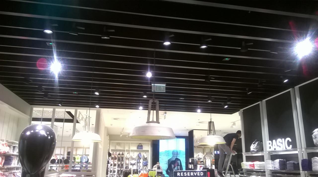 Czarny sufit rastrowy z oświetleniem punktowym w salonie RESERVED CH MOKOTÓW, widoczny fragment instalacji elektrycznej i system wentylacji, w tle ekspozycja sklepu z odzieżą.