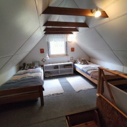 Mały Domek na Kaszubach - Pokój na poddaszu z dwoma pojedynczymi łóżkami, białą komodą pod oknem i drewnianymi belkami stropowymi. Ustawny pokój w pensjonacie.