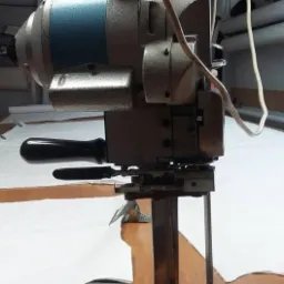 Elektryczny n&oacute;ż krojczy na stole z rozłożonym białym materiałem, widoczne metalowe elementy i czarny uchwyt.