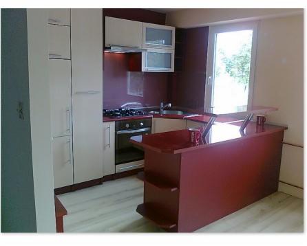 Nowoczesna kuchnia z zabudową w odcieniach bieli i burgundu, z wyspą kuchenną i widokiem na okno.