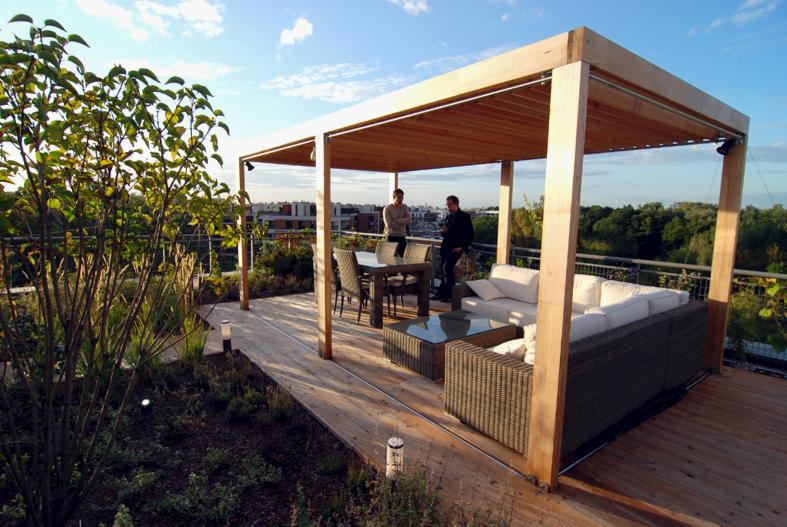 Ogród na dachu z drewnianą pergolą, meblami ogrodowymi i dwoma mężczyznami w tle, widok na miasto.