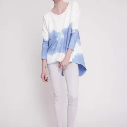 Modelka prezentuje bawełnianą bluzę Blue Cloud z efektem tie-dye, białe spodnie i czarne botki na białym tle.