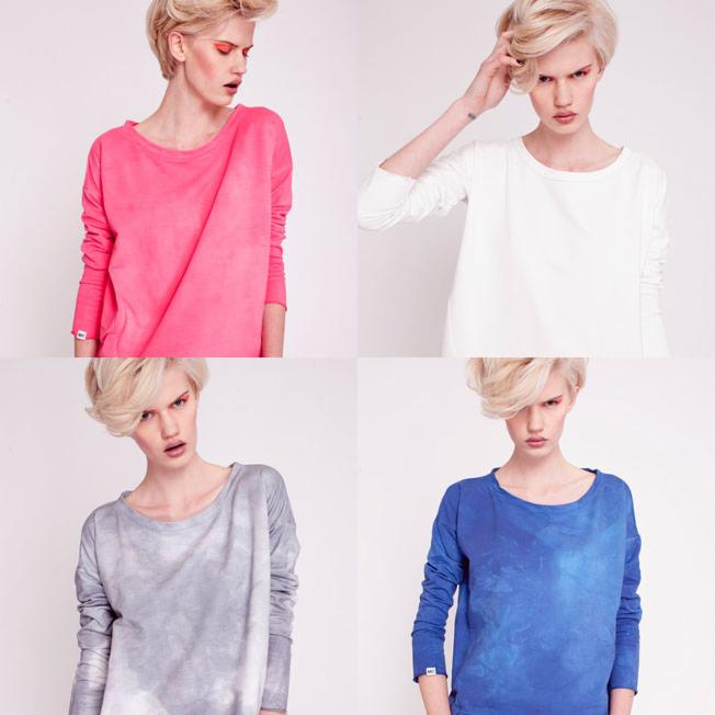 Kolaż czterech zdjęć modelki w bawełnianych bluzach basic w kolorach: różowym, białym, szarym i niebieskim, na białym tle, z widocznym znakiem firmowym na dole.