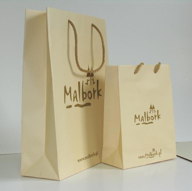 Dwie beżowe papierowe torby z brązowymi uchwytami sznurkowymi i nadrukiem 'Malbork' z sylwetką zamku, na białym tle.