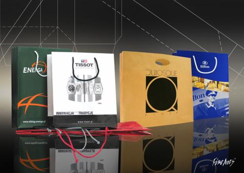 Cztery papierowe torby reklamowe z nadrukami firmowymi (Energa, Tissot, Quiosque, Hilton) stojące na błyszczącej powierzchni, widoczne odbicie.