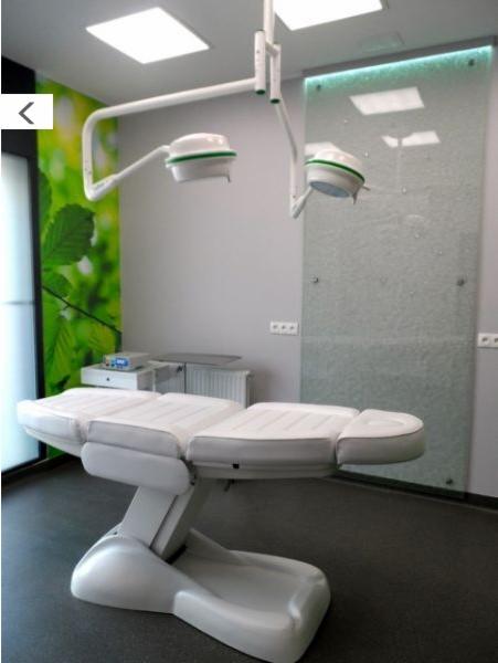 Nowoczesny gabinet lekarski z regulowanym fotelem zabiegowym, oświetleniem operacyjnym i dekoracyjną szklaną ścianą z podświetleniem.