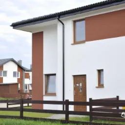 Dwukondygnacyjny dom jednorodzinny z brązowymi akcentami na elewacji, widoczny zza drewnianego płotu; w tle inne domy w zabudowie szeregowej.