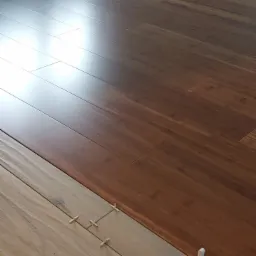 Fragment podłogi z ułożonymi panelami w dwóch odcieniach drewna, z widocznymi krzyżykami dystansowymi przy jasnych panelach.