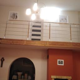 Dod-met - Wnętrze domu z antresolą zabezpieczoną nowoczesną balustradą ze stali nierdzewnej z poziomymi prętami, widok od dołu na drewnianą konstrukcję antresoli i dekoracje ścienne.