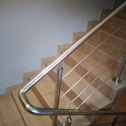 Dod-met - Metalowa poręcz schodowa z wypełnieniem prętami, zamontowana na schodach wyłożonych płytkami imitującymi drewno, widok z góry.