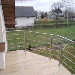 Dod-met - Balkon z jasnymi płytkami i nowoczesną, metalową barierką z widokiem na ogród i zabudowania w tle.