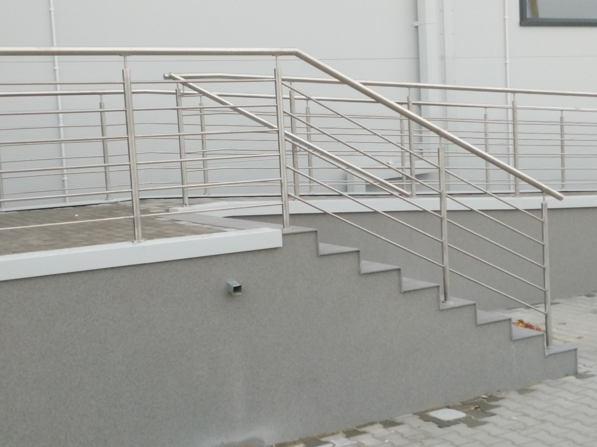 Zewnętrzne schody z szarą elewacją i balustradą ze stali nierdzewnej z poziomymi prętami, widok z boku.