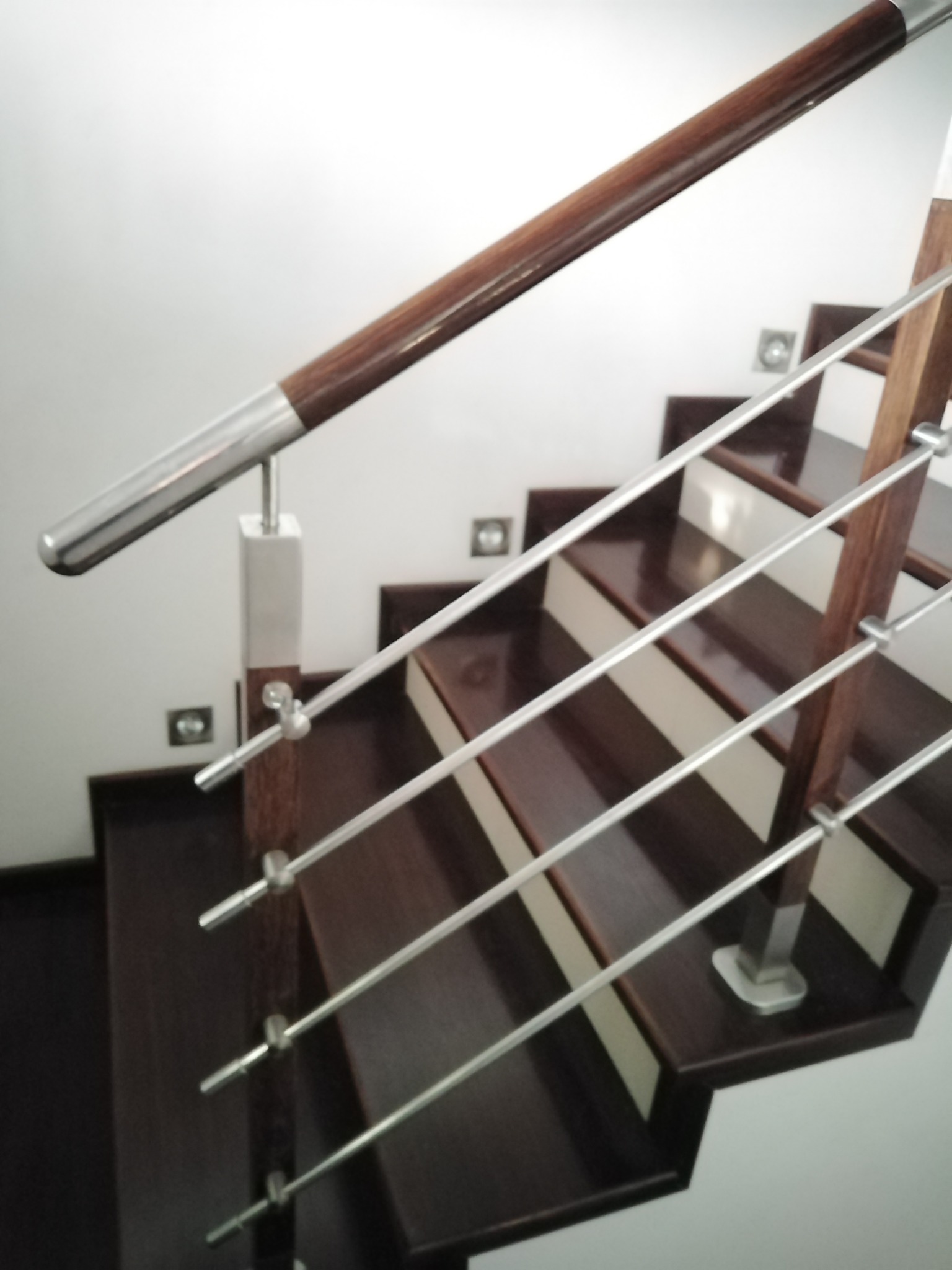 Nowoczesne schody z ciemnego drewna z metalowymi prętami i drewnianą poręczą, widok z góry, detale mocowania prętów do słupków.