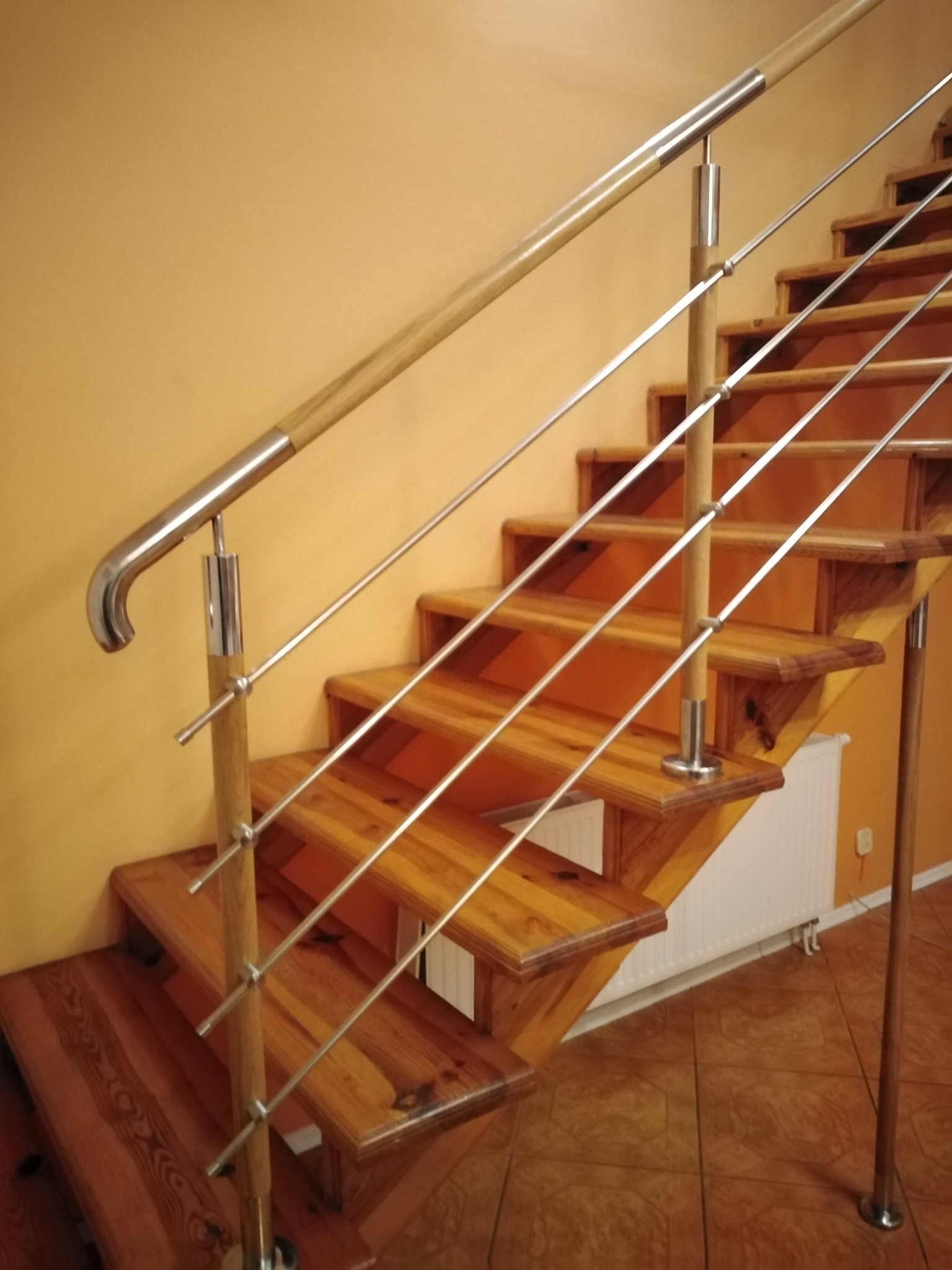 Drewniane schody z metalowymi poręczami i balustradami ze stali nierdzewnej, widok z dołu ukazujący konstrukcję i detale wykończenia.