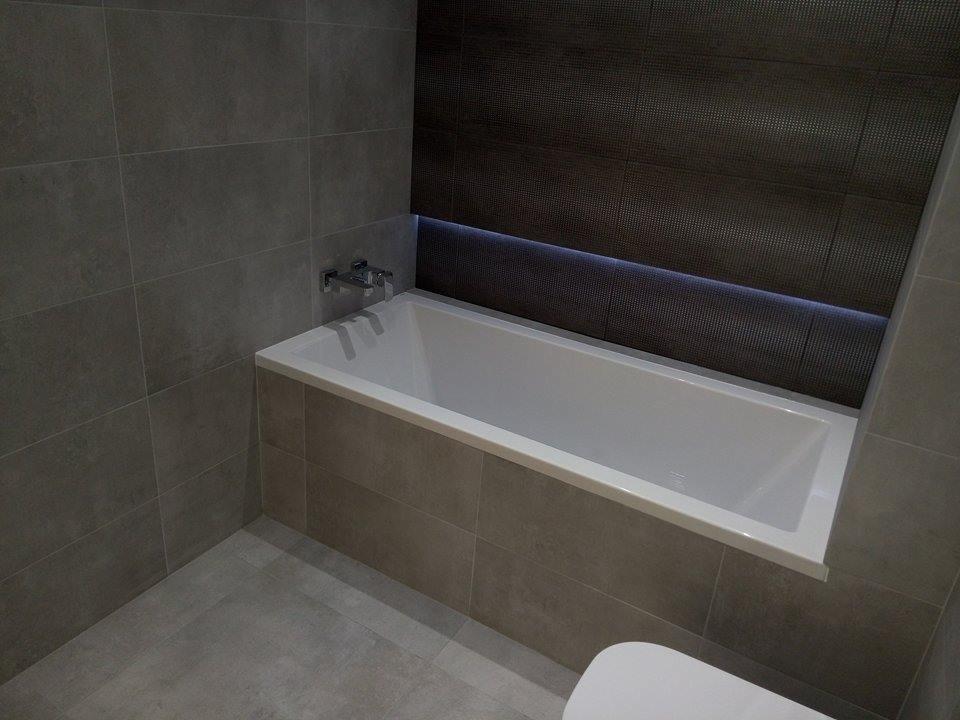 Nowoczesna łazienka z wanną obudowaną szarą płytką, chromowana bateria, ciemna mozaika z podświetleniem LED na ścianie