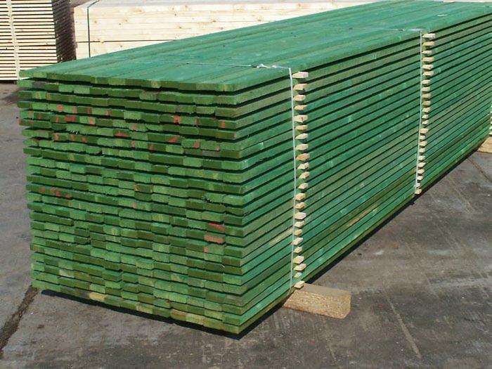 Stos impregnowanych na zielono desek tarcicy ułożonych warstwami, zabezpieczonych sznurkiem, z widocznymi znakami identyfikacyjnymi na niektórych deskach.