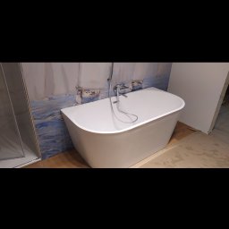 REMONTY I WYKOŃCZENIA DOMÓW I MIESZKAŃ Arkadiusz Ruszkowski - Wolnostojąca wanna w łazience z motywem morskim na ścianie. Bateria wannowa zamontowana na wannie. Widoczny fragment kabiny prysznicowej.