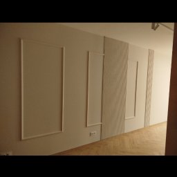 REMONTY I WYKOŃCZENIA DOMÓW I MIESZKAŃ Arkadiusz Ruszkowski - Ściana z dekoracyjnymi panelami i listwami w jasnym wnętrzu. Widoczne gniazdka elektryczne i parkiet ułożony w jodełkę. Minimalistyczny design.