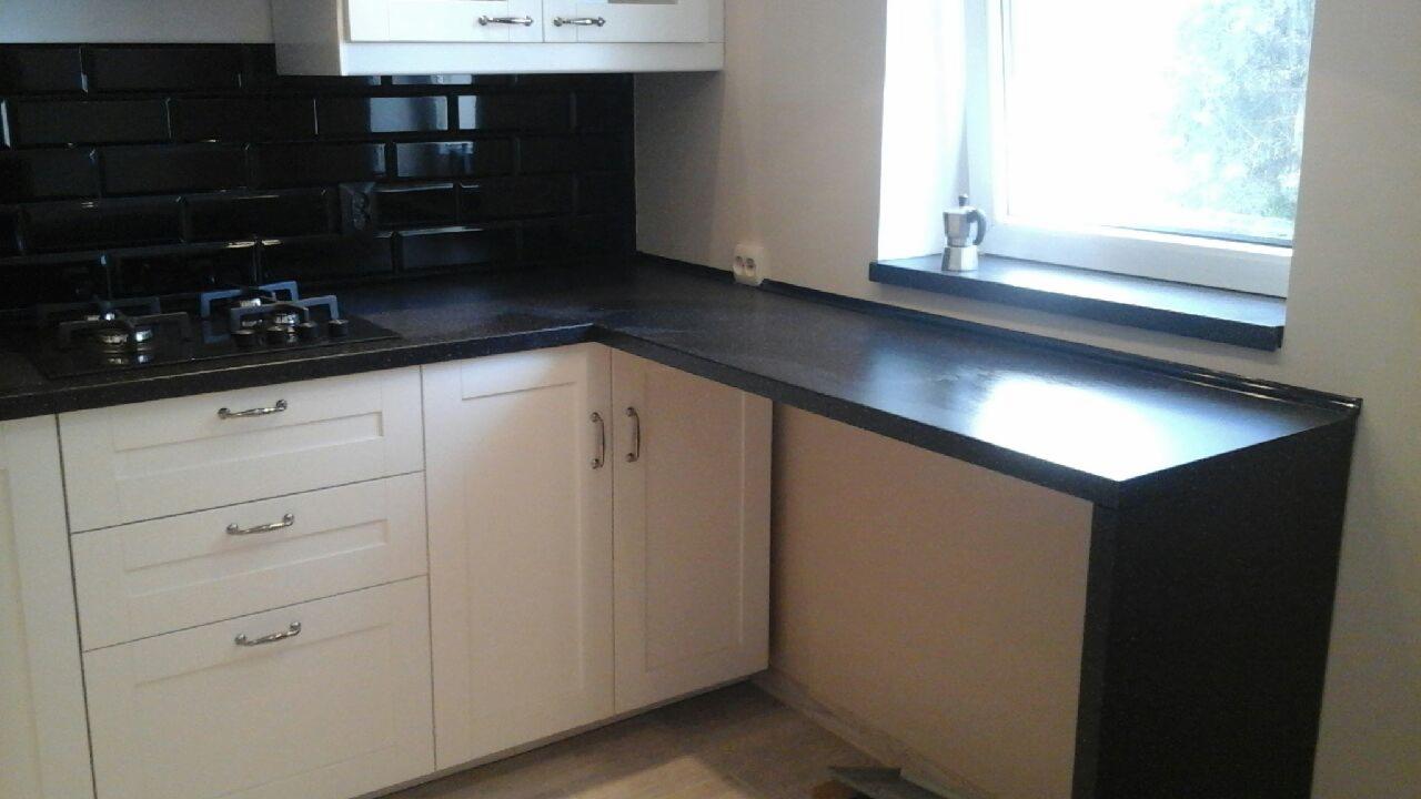 Wykończona kuchnia z czarnym blatem i płytkami, białymi szafkami z szufladami i oknem z metalowym zaparzaczem do kawy.