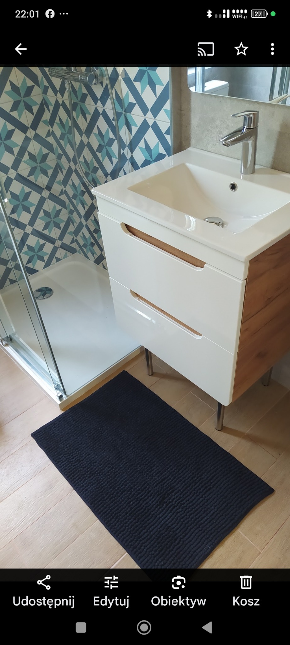 Nowoczesna łazienka z kabiną prysznicową, umywalką z szafką w odcieniach bieli i drewna oraz niebiesko-białymi płytkami w geometryczny wzór na ścianie.