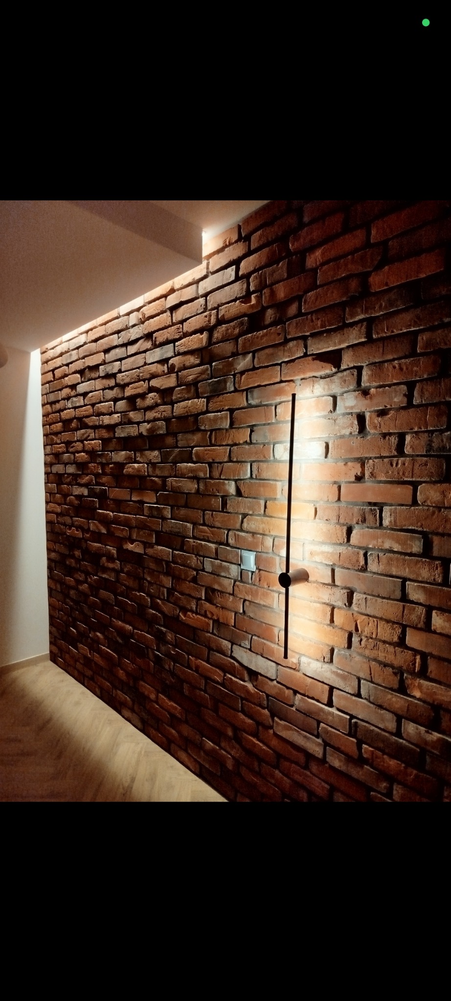 Ceglana ściana z oświetleniem LED wzdłuż krawędzi sufitu i minimalistyczną lampą ścienną. Dekoracyjne wykończenie wnętrza z efektem starej cegły.