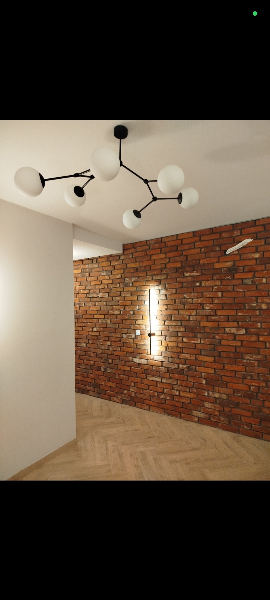Nowoczesna lampa sufitowa z białymi kulami oświetla ceglaną ścianę z pionowym oświetleniem i parkietem ułożonym w jodełkę w wykończonym wnętrzu.