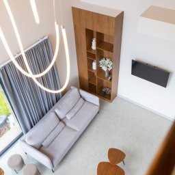 PPUH Art-Rad - Nowoczesny salon z antresoli: beżowa sofa, drewniany regał, telewizor na ścianie, designerskie lampy i stoliki kawowe. Widok z góry.