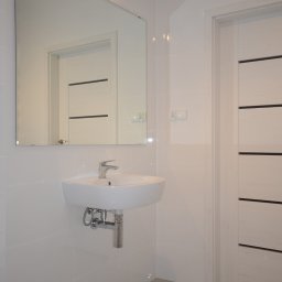 PPUH Art-Rad - Biała, nowoczesna łazienka z wiszącą umywalką, dużym lustrem i drzwiami z poziomymi panelami. Szare płytki podłogowe i błyszczące, białe płytki ścienne.