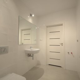 PPUH Art-Rad - Biała łazienka po remoncie: umywalka, lustro, grzejnik drabinkowy, płytki na ścianach i podłodze. Minimalistyczny design, czystość i nowoczesność.