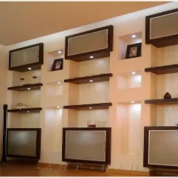 Ściana z wnękami oświetlonymi punktowo, z p&oacute;łkami w kolorze ciemnego drewna i szafkami z matowymi drzwiczkami, eksponująca dekoracje.