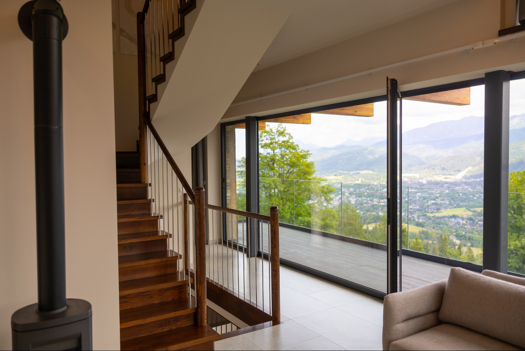 Nowoczesne wnętrze z drewnianymi schodami i panoramicznym oknem z widokiem na góry. Minimalistyczny design, jasne kolory, kominek.