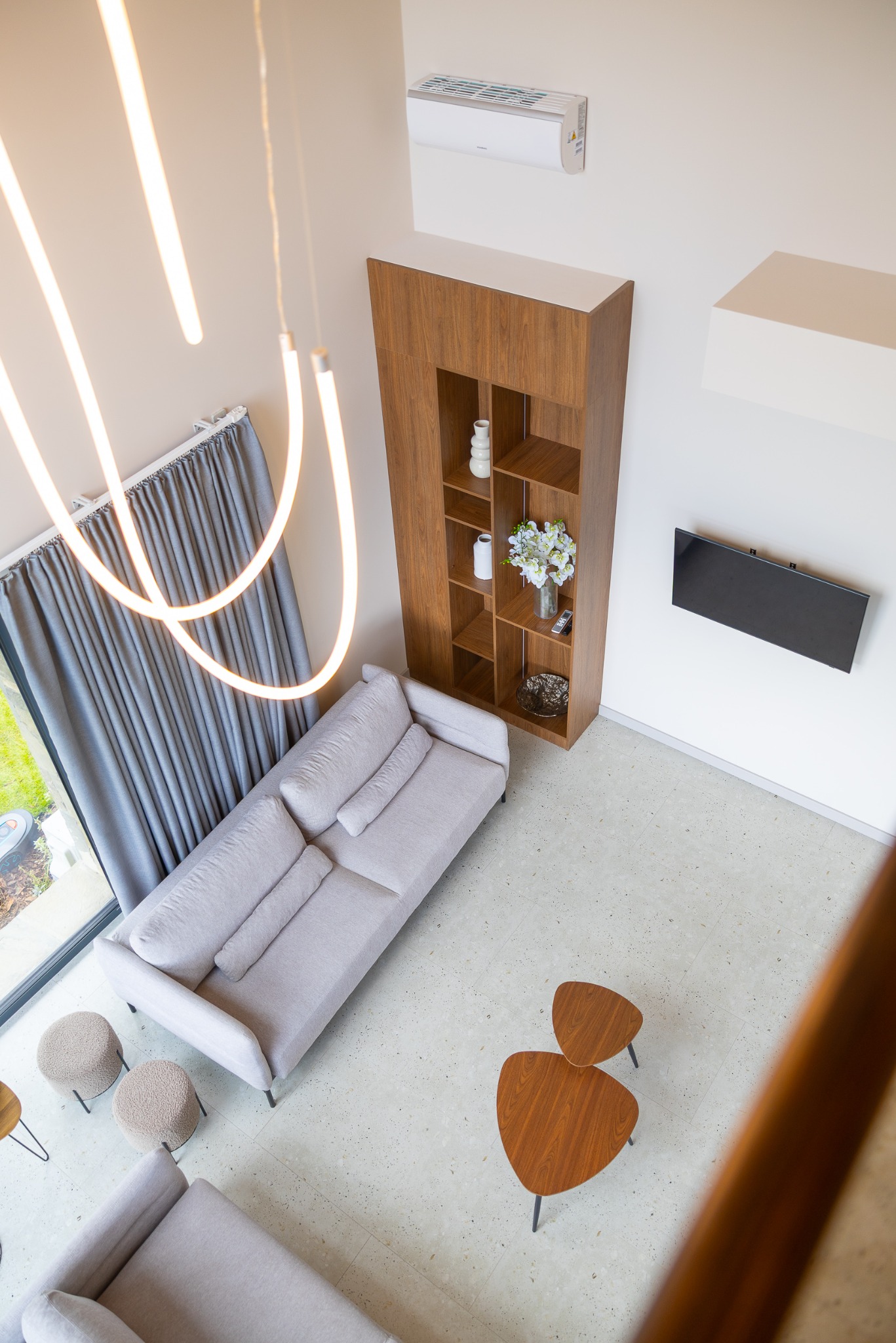 Nowoczesny salon z antresoli: beżowa sofa, drewniany regał, telewizor na ścianie, designerskie lampy i stoliki kawowe. Widok z góry.