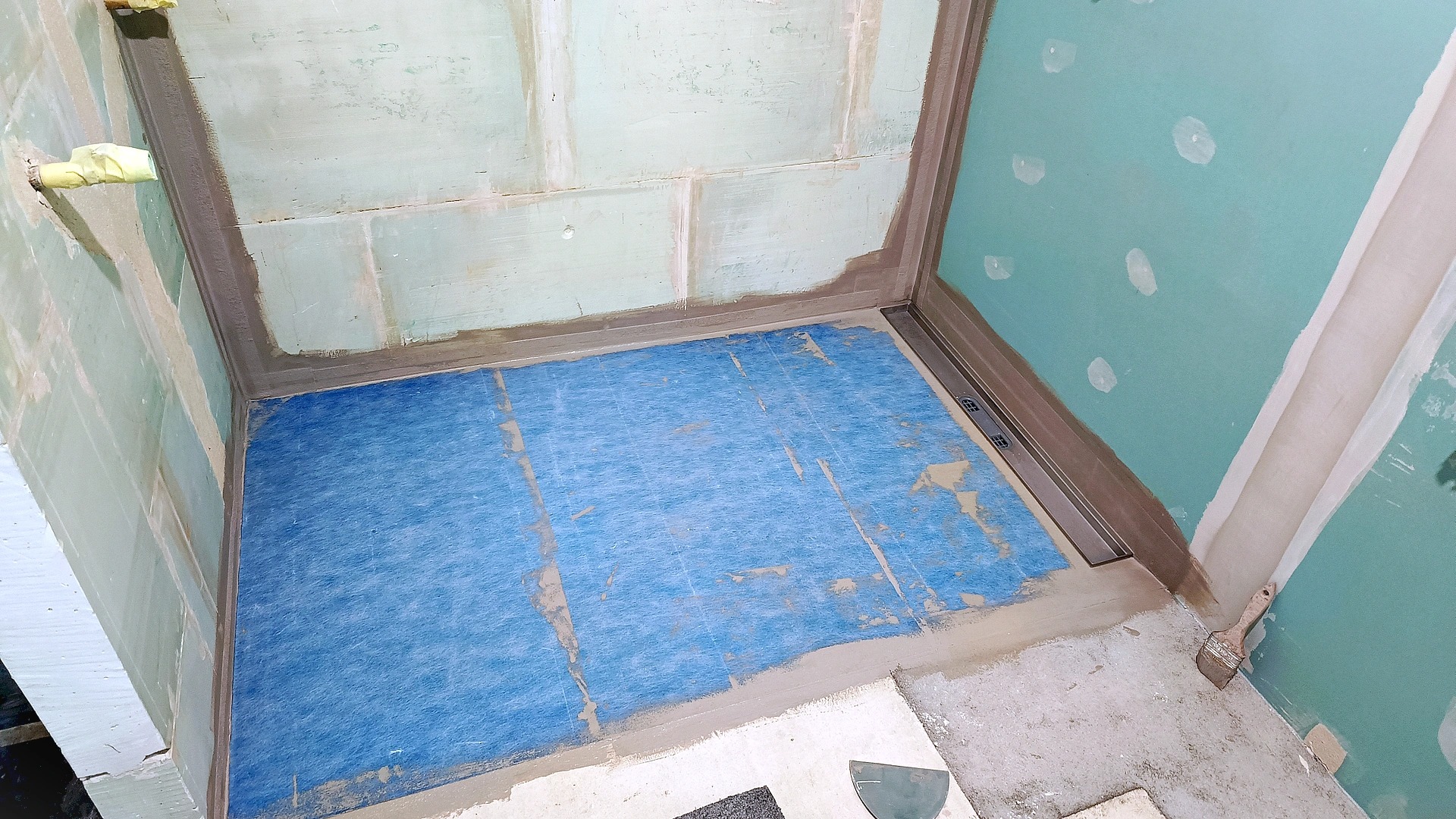 Hydroizolacja w kabinie prysznicowej we Wrocławiu. Widoczna niebieska mata hydroizolacyjna na podłodze i uszczelnione ściany, przygotowane do dalszych prac wykończeniowych.